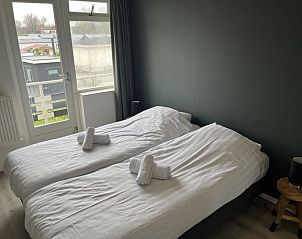 Slaapkamer met twee bedden in Vakantiehuis Groepsaccommodatie 12, Hellevoetsluis, met balkon en uitzicht op de omgeving.
